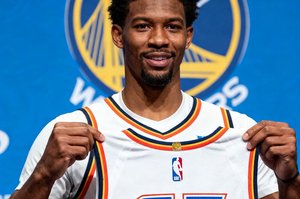 NBA休赛期转会新闻配图，一名球星身着新球队球衣在新闻发布会上展示球衣号码，背景板显示球队标志